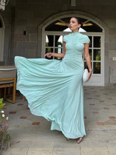 Woman in a light blue dress standing in an outdoor setting with a building in the background.